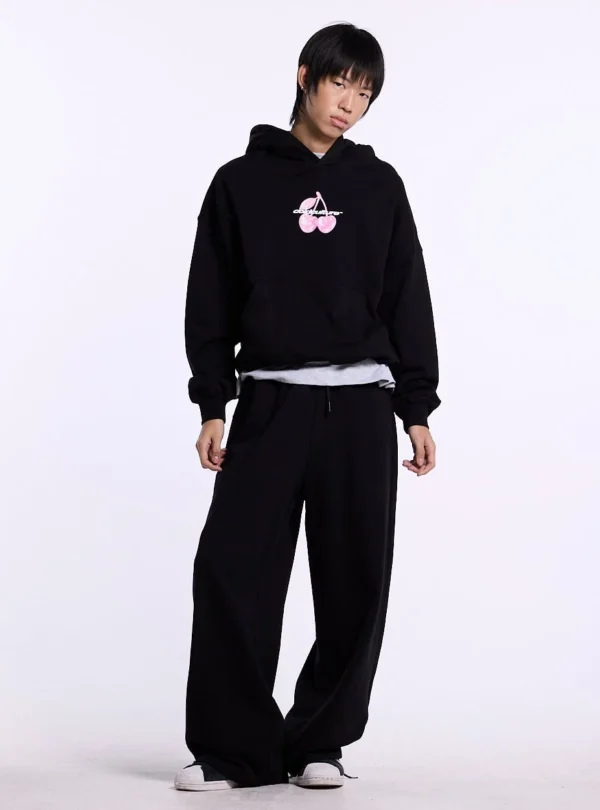 Modelo con sudadera negra Cold Culture Berry de frente con gráfico de cerezas rosas y bolsillo canguro