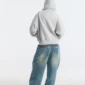 Vista trasera de modelo con sudadera Bands de Cold Culture en gris jaspeado, capucha estampada puesta y corte holgado combinado con vaqueros anchos.
