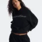 Modelo luciendo la sudadera negra Bling de Cold Culture para mujer, con detalle del logotipo brillante, bolsillo canguro y mangas amplias.