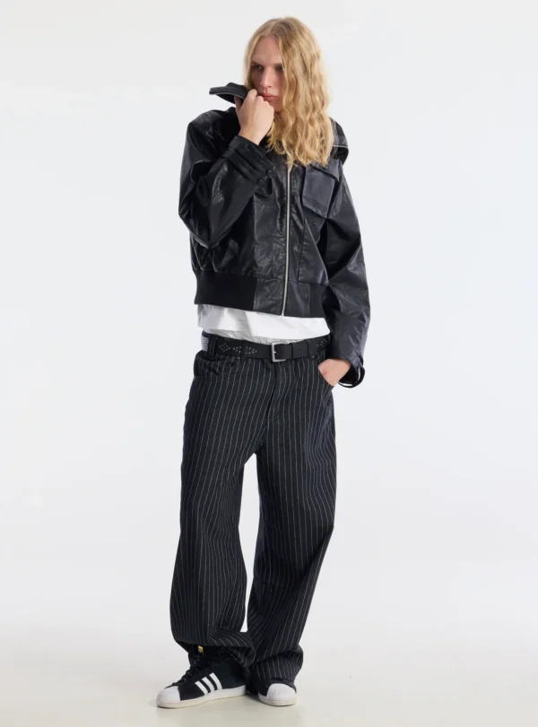 Modelo de cuerpo entero con el abrigo negro Bunker Bomber de Cold Culture, cremallera frontal y pantalones oscuros de rayas.