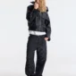 Modelo de cuerpo entero con el abrigo negro Bunker Bomber de Cold Culture, cremallera frontal y pantalones oscuros de rayas.