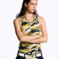 Modelo con los brazos cruzados luciendo la camiseta de tirantes Camo Tank Top amarilla de Cold Culture, con estampado de camuflaje y logotipo blanco, combinada con vaqueros oscuros