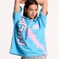 Modelo con polo Cocky azul de Cold Culture, brazos levantados, mostrando el diseño frontal con letras blancas, contornos morados y franja rosa diagonal.
