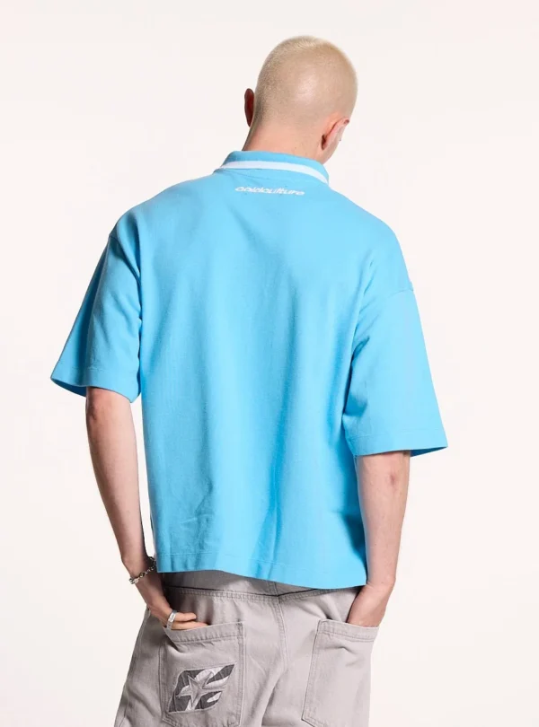 Modelo de espaldas con el polo Cocky azul de Cold Culture, mostrando su corte holgado, hombros caídos y pequeño logotipo blanco en la parte superior.
