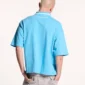 Modelo de espaldas con el polo Cocky azul de Cold Culture, mostrando su corte holgado, hombros caídos y pequeño logotipo blanco en la parte superior.