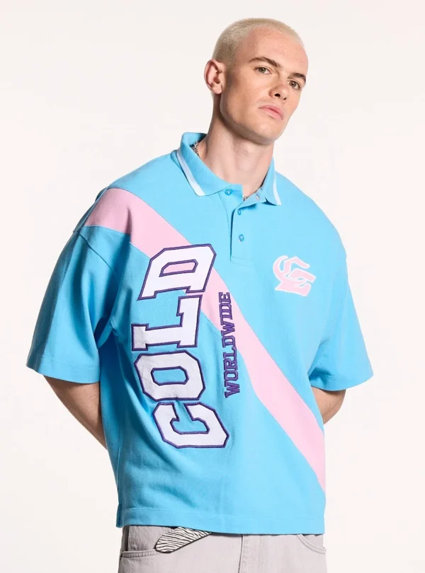 Modelo luciendo el polo Cocky azul de Cold Culture con corte oversize, franja diagonal rosa y letras grandes COLD WORLDWIDE en el frontal.