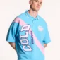 Modelo luciendo el polo Cocky azul de Cold Culture con corte oversize, franja diagonal rosa y letras grandes COLD WORLDWIDE en el frontal.