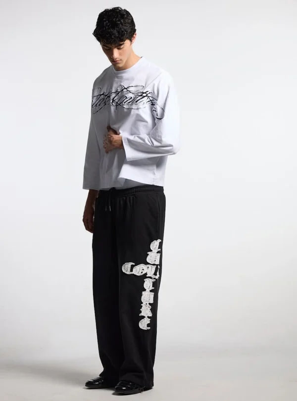 Modelo con pantalones deportivos negros Cold Culture Crossed, de corte ancho y gráfico blanco en la pernera