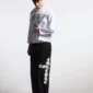 Modelo con pantalones deportivos negros Cold Culture Crossed, de corte ancho y gráfico blanco en la pernera