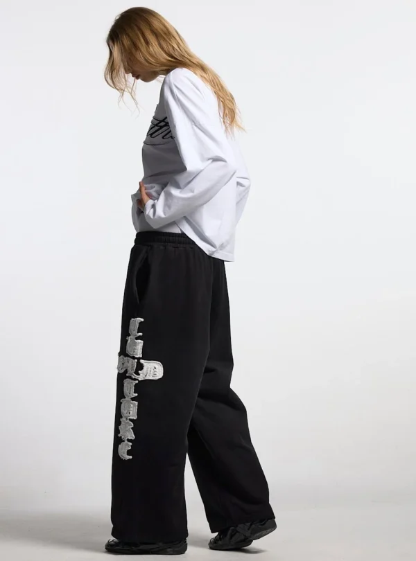 Vista lateral de modelo con pantalones deportivos negros Cold Culture Crossed y gráfico blanco en la pernera
