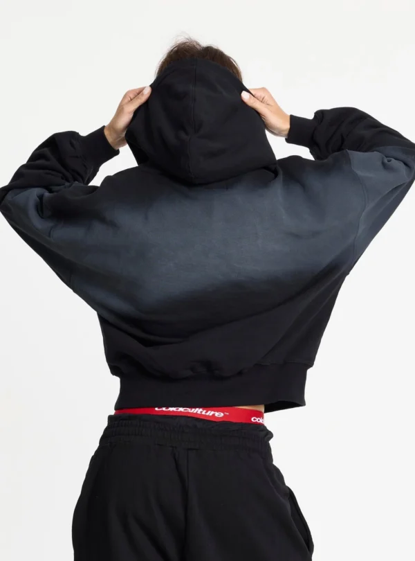 Cold Culture Crossed Sudadera Black – Detalle trasero de la capucha Modelo de espaldas sujetando la capucha de la sudadera Crossed Black de Cold Culture, con degradado gris y puños y cintura de canalé.