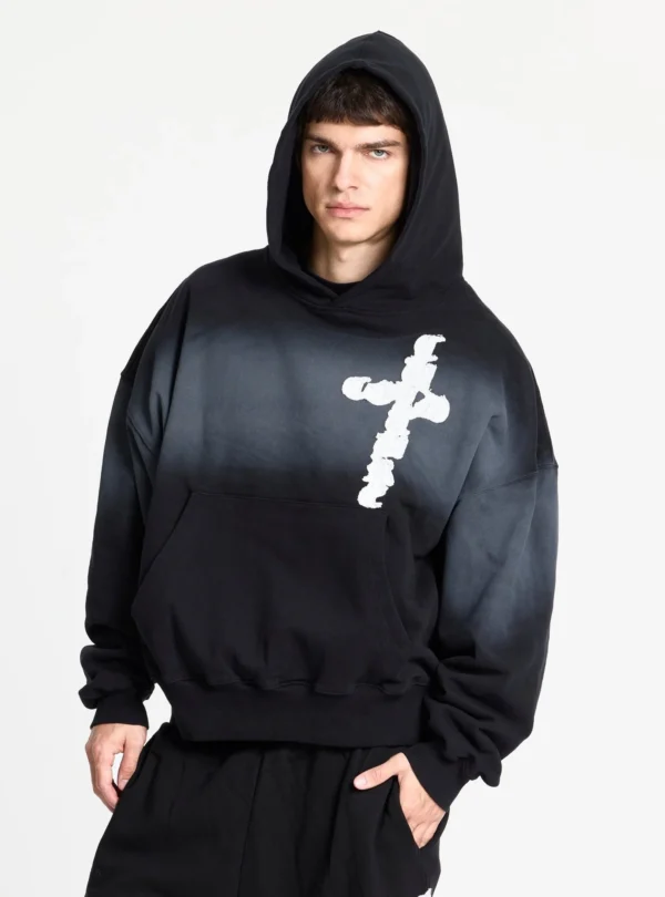 Cold Culture Crossed Sudadera Black – Vista frontal con capucha puesta Modelo con sudadera Crossed Black de Cold Culture, capucha puesta, gráfico blanco de cruz en el pecho, mangas amplias y bolsillo canguro.
