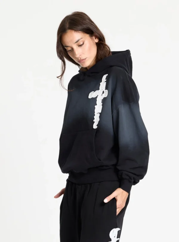 Cold Culture Crossed Sudadera Black – Vista tres cuartos con modelo Modelo con sudadera negra Crossed de Cold Culture, capucha, efecto degradado gris, gráfico blanco en forma de cruz y bolsillo canguro.