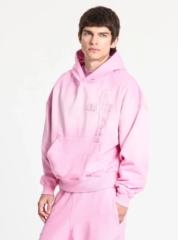Cold Culture Crossed Sudadera Pink – Vista de tres cuartos con modelo Modelo con la sudadera rosa Crossed de Cold Culture en vista de tres cuartos, con capucha, bolsillo canguro y diseño de cruz en relieve.