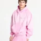 Modelo con la sudadera rosa Crossed de Cold Culture en vista de tres cuartos, con capucha, bolsillo canguro y diseño de cruz en relieve.