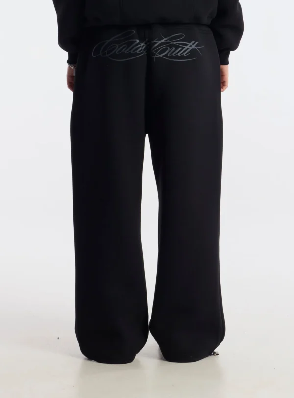 Detalle trasero de los pantalones deportivos Curve negros de Cold Culture puestos por una modelo, con logotipo grande en tipografía cursiva gris.