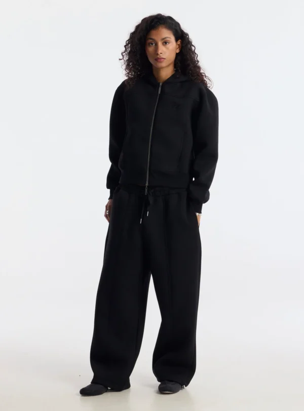 Modelo de frente con pantalones deportivos Curve negros de Cold Culture, de corte holgado y pernera ancha, combinados con sudadera negra.