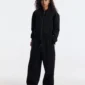 Modelo de frente con pantalones deportivos Curve negros de Cold Culture, de corte holgado y pernera ancha, combinados con sudadera negra.