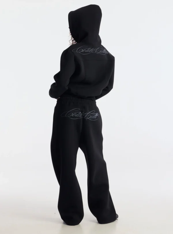 Modelo de espaldas con pantalones deportivos Curve negros de Cold Culture, con pernera ancha y logotipo de la marca en la parte trasera.