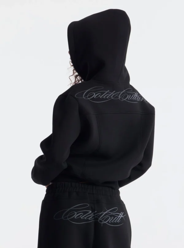 Detalle trasero de la sudadera Curve Zip-up Hoodie negra de Cold Culture, con logotipo en tipografía cursiva sobre los hombros y capucha puesta.