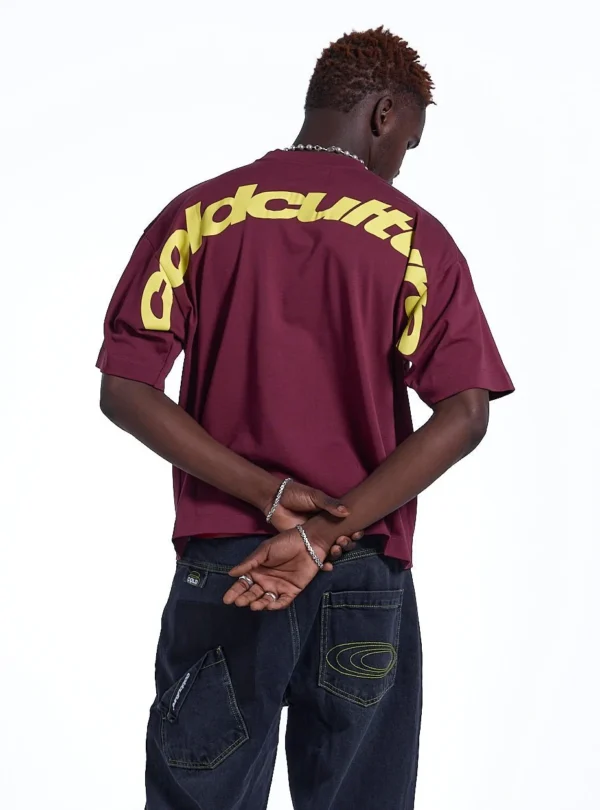 Modelo con camiseta Cold Culture Curved en burdeos y amarillo, vista trasera con gráfico de Cold Culture sobre hombros y mangas