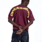 Modelo con camiseta Cold Culture Curved en burdeos y amarillo, vista trasera con gráfico de Cold Culture sobre hombros y mangas