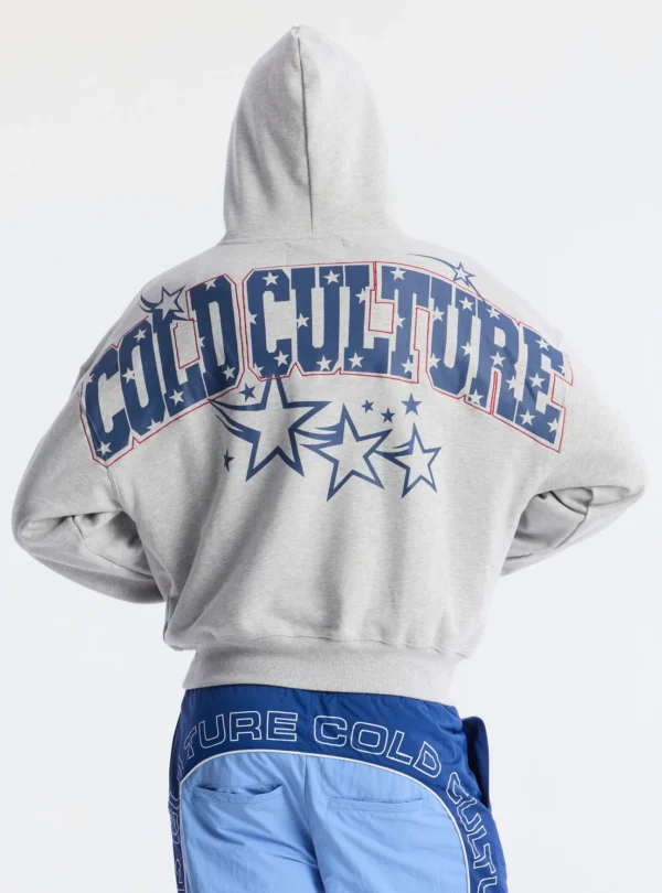 Vista de espalda de un modelo con la sudadera Fourth Of July de Cold Culture en gris jaspeado, mostrando el gran estampado azul con estrellas y letras de la marca.