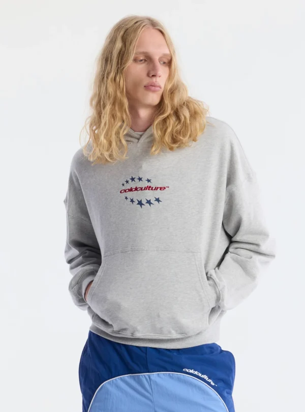 Modelo con sudadera Fourth Of July de Cold Culture en gris jaspeado, de corte holgado, con capucha, logotipo rojo y estrellas azules en el pecho.