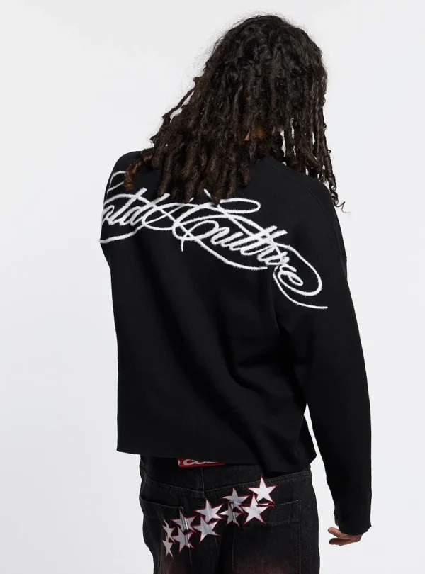Modelo de espaldas con jersey negro Furry Script Knit de Cold Culture, mostrando el gran logotipo blanco de estilo caligráfico que ocupa la parte superior de la espalda.
