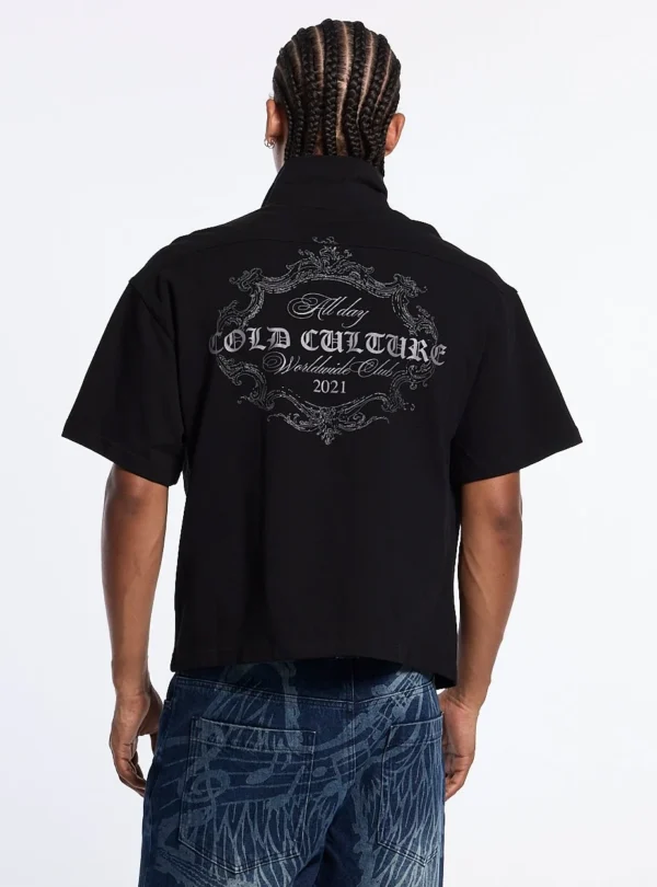 Modelo de espaldas vistiendo el Gilded Polo negro de Cold Culture, con un gran estampado ornamental gris y letras Cold Culture Worldwide Club 2021.