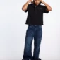 Modelo de cuerpo entero vistiendo el Gilded Polo negro de Cold Culture con vaqueros anchos azules y sujetando el cuello del polo.