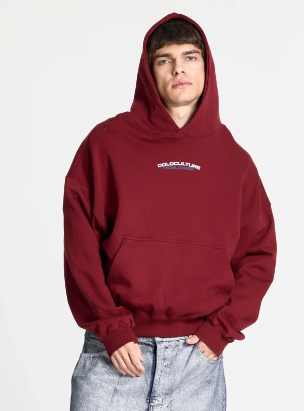 Modelo con sudadera Holeshot Burgundy de Cold Culture, capucha puesta, corte holgado, bolsillo canguro y logotipo en el pecho.
