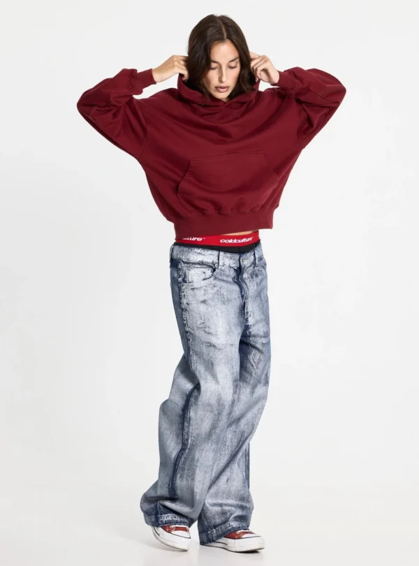 Modelo luciendo la sudadera Holeshot Burgundy de Cold Culture con corte holgado y bolsillo canguro, mientras se ajusta la capucha.