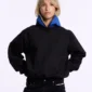 Modelo con sudadera sin capucha Cold Culture Intercept en negro y azul marino, mostrando la capucha azul abierta y el logotipo del pecho