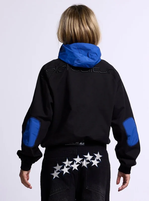 Vista trasera en modelo de la sudadera sin capucha Cold Culture Intercept en negro y azul marino, con capucha y coderas azules y logotipo bordado