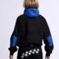 Vista trasera en modelo de la sudadera sin capucha Cold Culture Intercept en negro y azul marino, con capucha y coderas azules y logotipo bordado