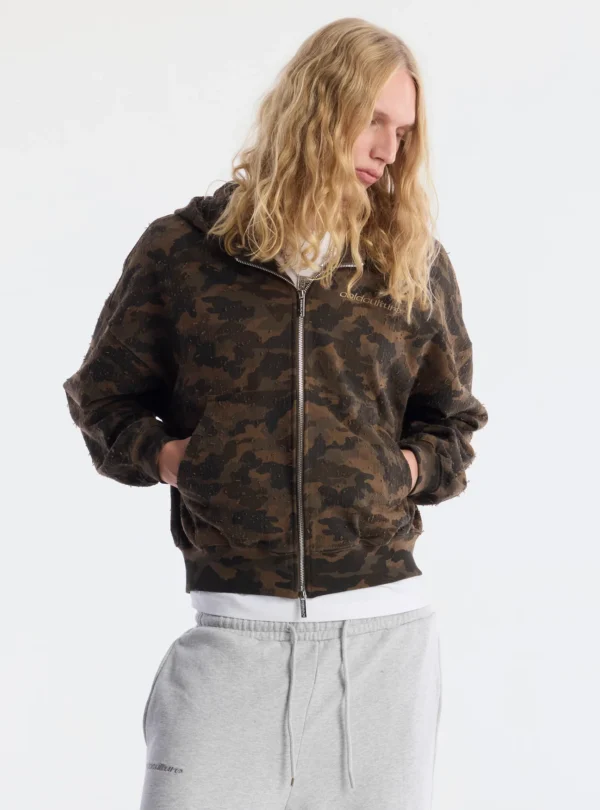 Modelo con sudadera Lead Zip-up Hoodie Camo de Cold Culture cerrada, con las manos en los bolsillos delanteros y logo discreto en el pecho.