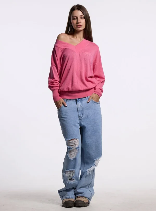 Cold Culture Lull Knit Mujer – Rosa – Vista frontal con modelo Modelo con jersey Lull Knit rosa de Cold Culture, escote en pico, hombro descubierto y mangas largas, combinado con vaqueros anchos.