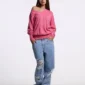 Modelo con jersey Lull Knit rosa de Cold Culture, escote en pico, hombro descubierto y mangas largas, combinado con vaqueros anchos.