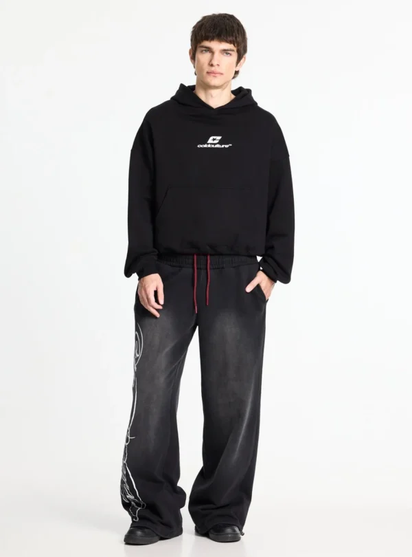 Cold Culture Nighthunt Pantalones Deportivos – Black – Modelo de frente Modelo con pantalones deportivos Cold Culture Nighthunt negros de corte ancho, gráfico blanco lateral y cordones rojos