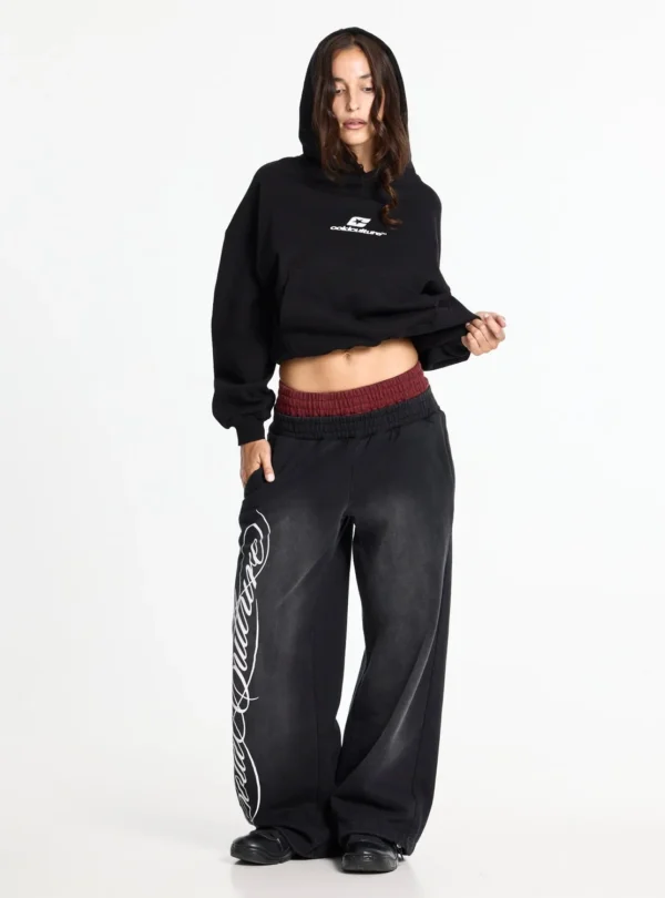 Cold Culture Nighthunt Pantalones Deportivos – Black – Vista frontal en modelo Modelo con pantalones deportivos Cold Culture Nighthunt negros, gráfico blanco en la pernera y cintura elástica roja