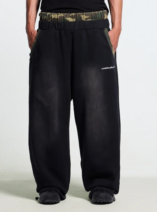 Detalle frontal de los pantalones deportivos Cold Culture OPS negros con cintura de camuflaje, bolsillos y logotipo blanco