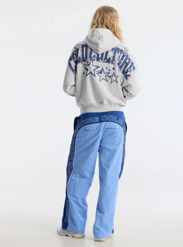 Vista de espalda de un modelo con pantalones deportivos Overcut de Cold Culture en azul, con estampado CULTURE COLD en la parte trasera y los laterales, combinados con una sudadera gris.