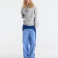 Modelo con pantalones deportivos Overcut de Cold Culture en azul, de corte ancho y paneles bicolor, combinados con una sudadera gris con capucha y zapatillas blancas.