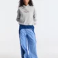 Modelo con pantalones deportivos Overcut de Cold Culture en azul claro y azul oscuro, con perneras anchas, ribetes blancos y estampado lateral, combinados con una sudadera gris y zapatillas deportivas.