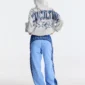 Vista trasera de una modelo con pantalones deportivos Overcut de Cold Culture en azul, con paneles bicolor, estampado CULTURE COLD en la cintura y los laterales, y perneras de corte ancho.