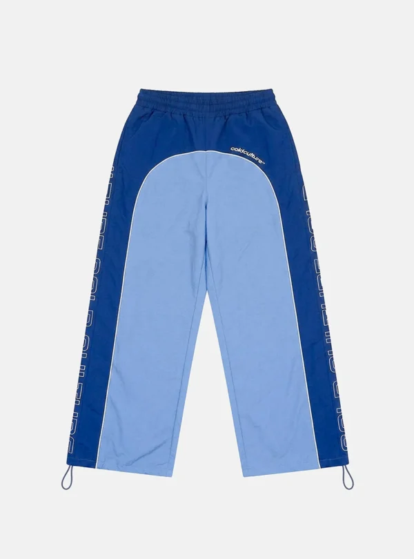 Vista frontal de los pantalones deportivos Overcut de Cold Culture en azul, con perneras anchas, paneles centrales azul claro, laterales azul oscuro, logotipo en la parte superior y cintura elástica.