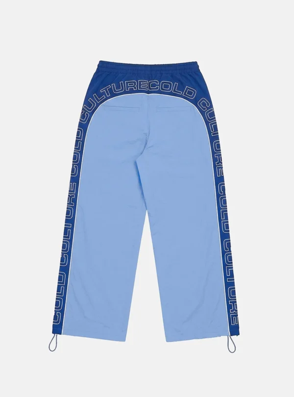 Vista trasera de los pantalones deportivos Overcut de Cold Culture en azul claro y azul oscuro, con estampado CULTURE COLD alrededor de la parte superior y los laterales, cintura elástica y bajos ajustables.