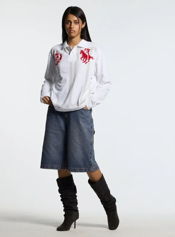 Cold Culture Pause Longsleeve Polo – Blanco – Look femenino frontal Modelo femenina con el polo blanco de manga larga Pause Longsleeve Polo de Cold Culture, combinado con bermudas vaqueras y botas negras altas.