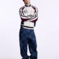 Modelo con jersey Pole Knit Off White de Cold Culture, con cremallera cerrada, mangas granates y blancas, combinado con vaqueros anchos azules.